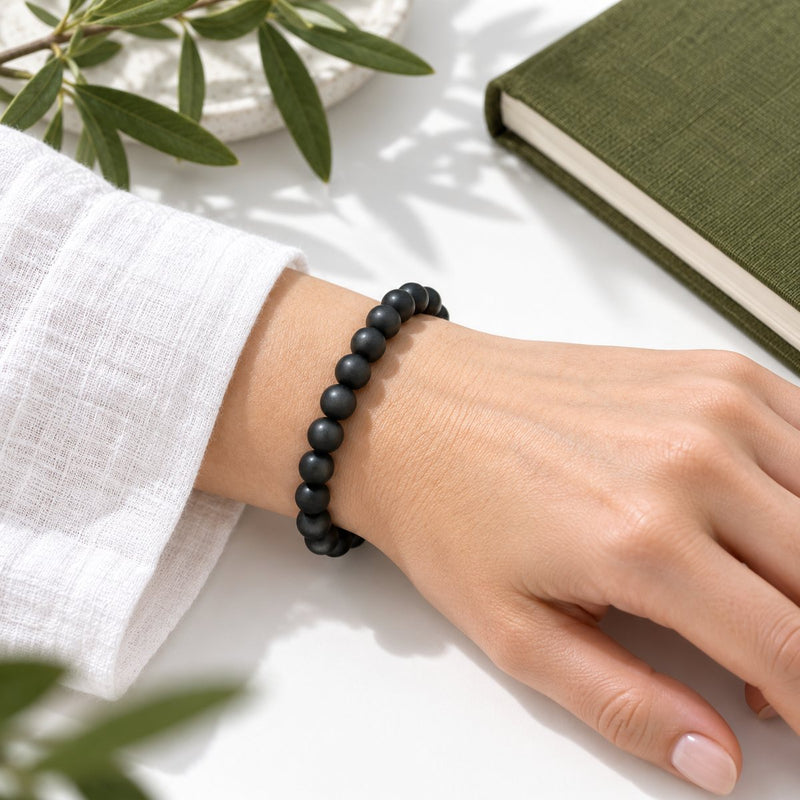 A matte shungite bead bracelet worn on the wrist beside a green notebook