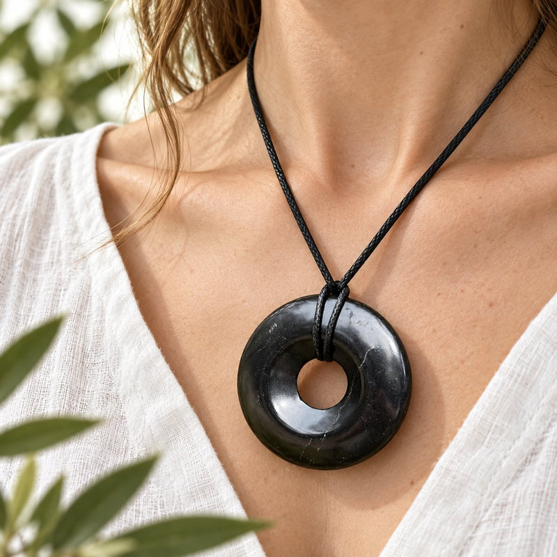 A polished shungite donut pendant worn on a black cord