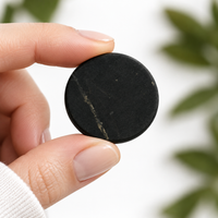 A single 20 mm shungite phone sticker held between finger and thumb