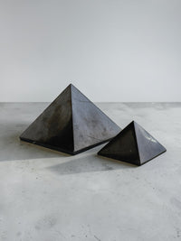 Shungite twin pyramids, 40 mm and 70 mm, on a grey surface