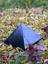 Small polished shungite pyramid outdoors on moss