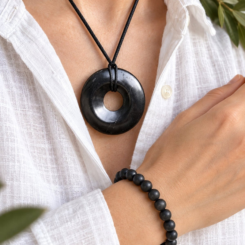 A shungite donut pendant and bead bracelet worn together over a white linen shirt